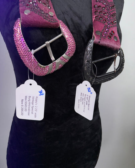 Two blinged-out belts with price tags on a burgandy Kippy